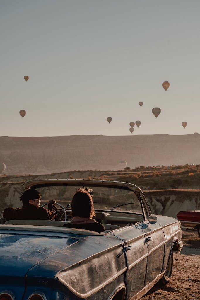 Couple enjoys scenic drive in vintage car with hot air balloons in Cappadocia, Turkey.