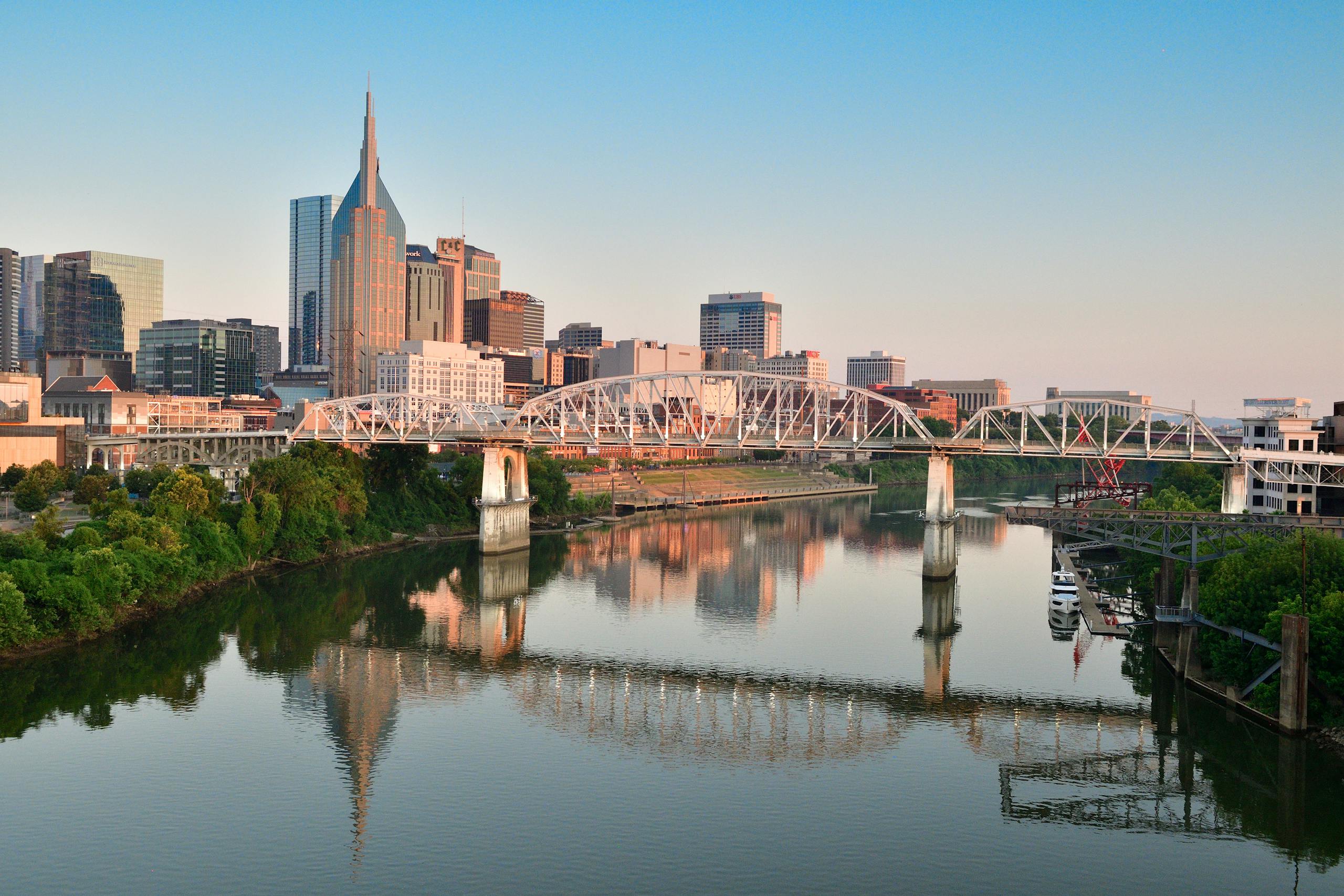 Scenic view of Nashville skyline and pedestrian bridge reflecting in the Cumberland River at sunrise.